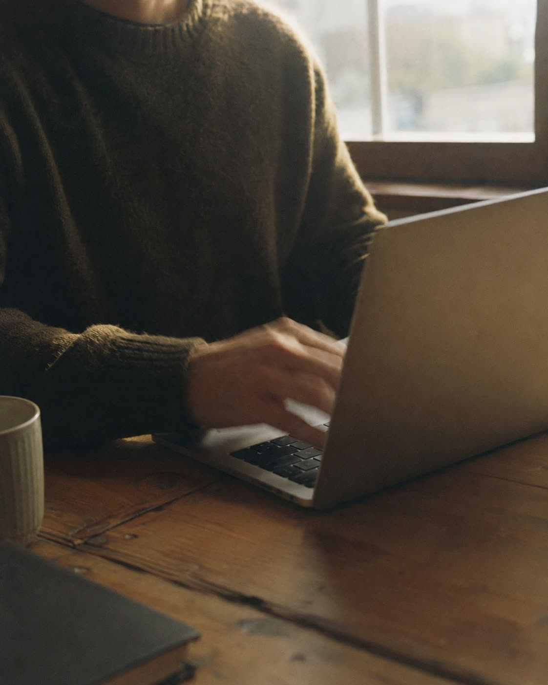 A person working at a laptop by a window in warm afternoon light